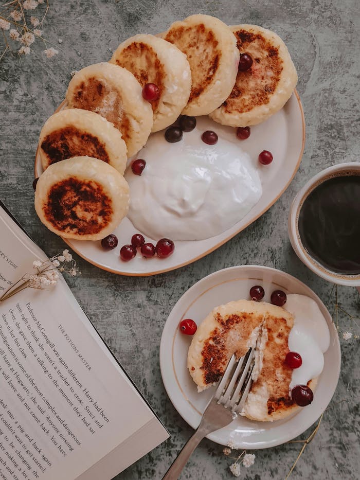heros-img Cozy breakfast scene featuring traditional syrniki with cranberries, yogurt, and a hot cup of coffee.