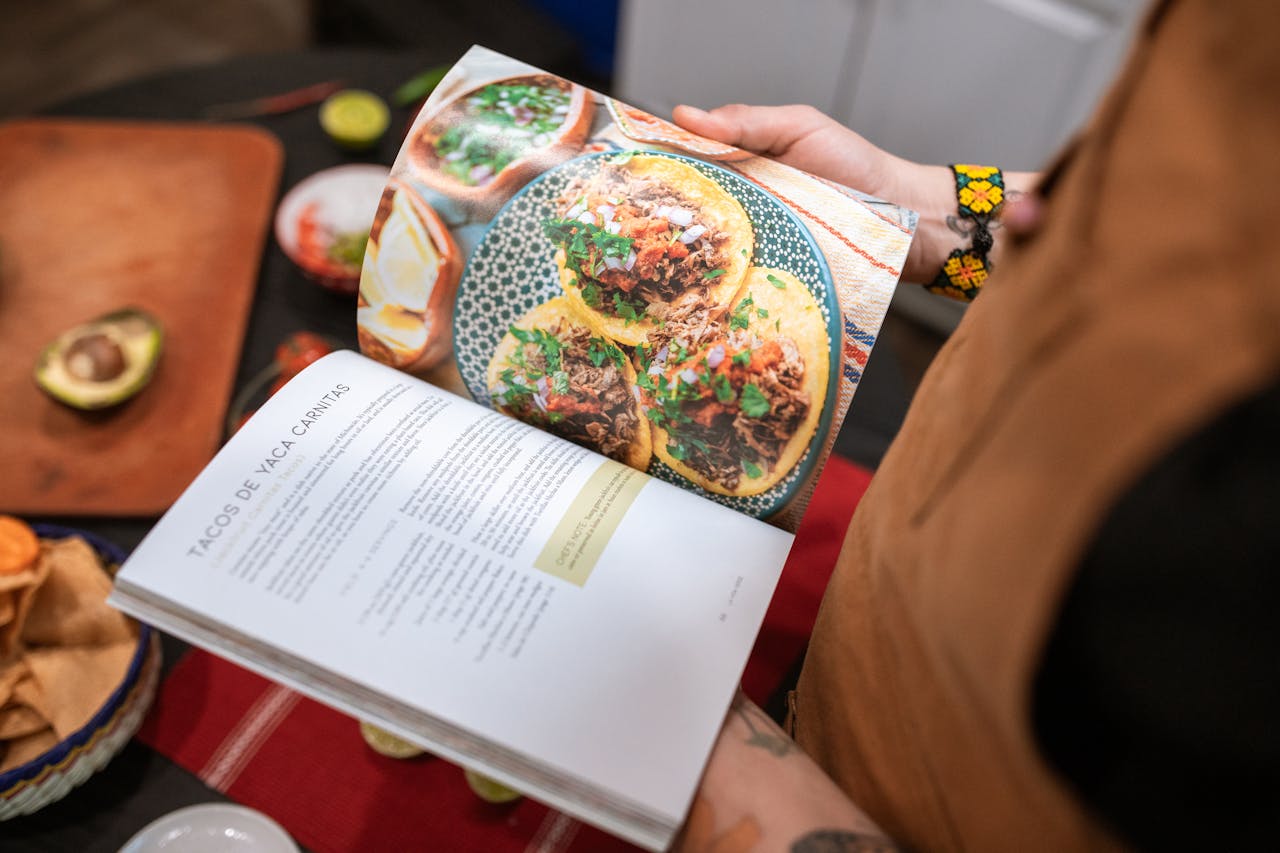 about-us A person holding a cookbook open to a delicious tacos recipe.